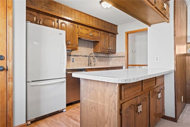 kitchen with a peninsula, light wood-style floors, stainless steel dishwasher, backsplash, and freestanding refrigerator