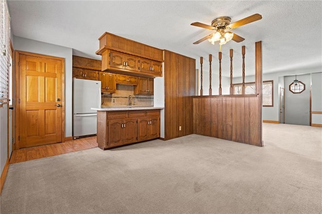 kitchen with light countertops, light colored carpet, brown cabinetry, freestanding refrigerator, and a sink