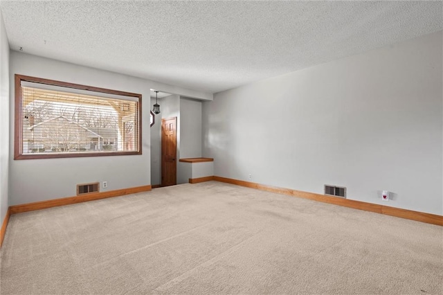 spare room featuring carpet, visible vents, a textured ceiling, and baseboards