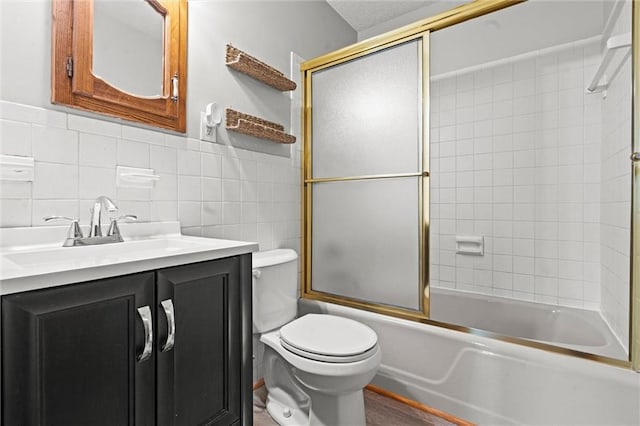 full bath with shower / bath combination with glass door, tile walls, toilet, wainscoting, and vanity