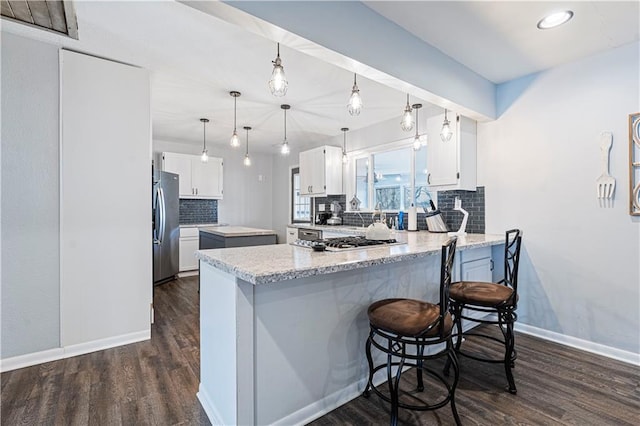 kitchen with tasteful backsplash, appliances with stainless steel finishes, a kitchen breakfast bar, kitchen peninsula, and white cabinets