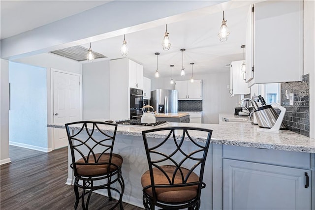 kitchen with appliances with stainless steel finishes, pendant lighting, white cabinetry, sink, and light stone countertops