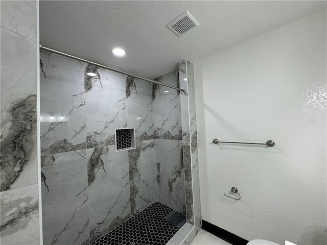 bathroom with a tile shower, a textured ceiling, and toilet