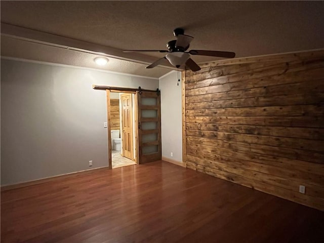 spare room with ceiling fan, a barn door, ornamental molding, a textured ceiling, and wood-type flooring