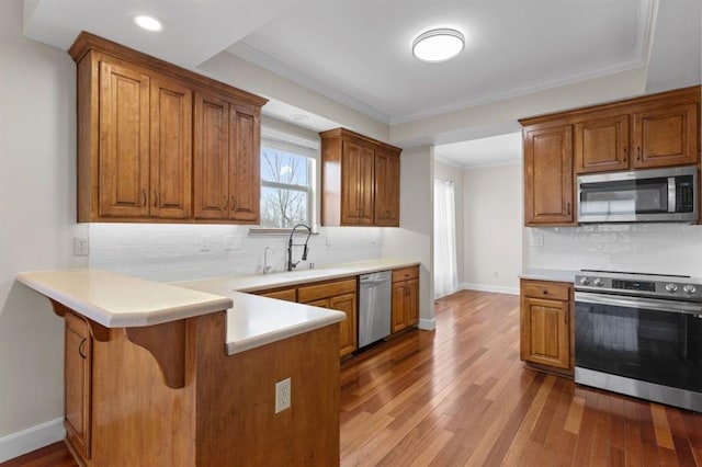 kitchen featuring appliances with stainless steel finishes, decorative backsplash, kitchen peninsula, crown molding, and light wood-type flooring