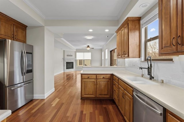 kitchen with appliances with stainless steel finishes, tasteful backsplash, wood-type flooring, sink, and ornamental molding