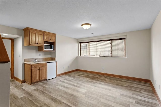 kitchen with white dishwasher, sink, a textured ceiling, and light wood-type flooring