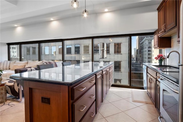 kitchen featuring dark stone counters, stainless steel appliances, sink, light tile patterned floors, and a center island