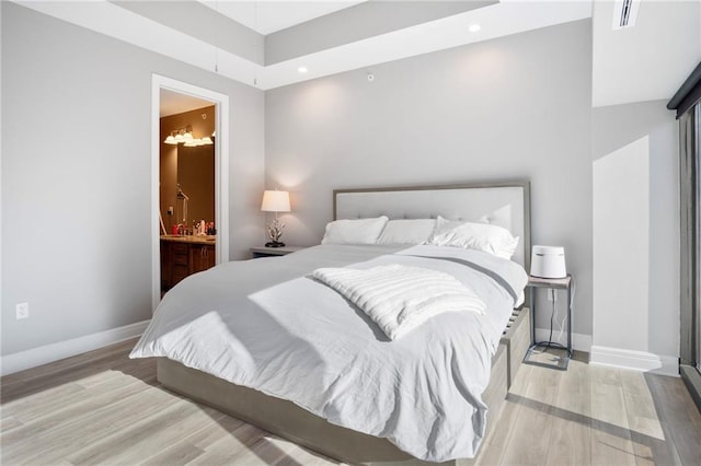 bedroom featuring connected bathroom and light hardwood / wood-style floors