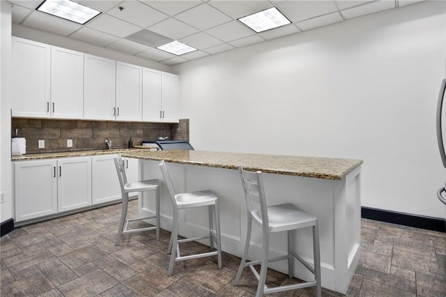 kitchen featuring a kitchen bar, backsplash, white cabinetry, and light stone countertops