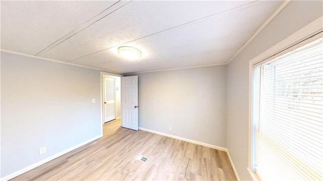 empty room with a textured ceiling, light wood-type flooring, and ornamental molding