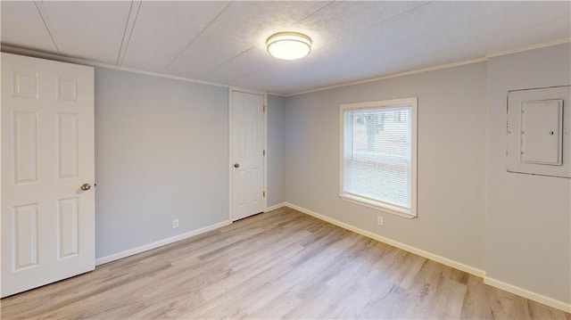 empty room with electric panel, ornamental molding, and light wood-type flooring