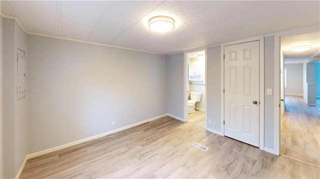 unfurnished bedroom with a closet, ensuite bathroom, crown molding, and light hardwood / wood-style floors