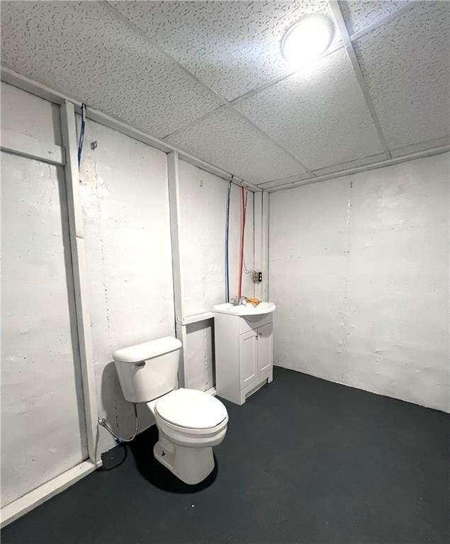 bathroom with a paneled ceiling, vanity, toilet, and concrete flooring