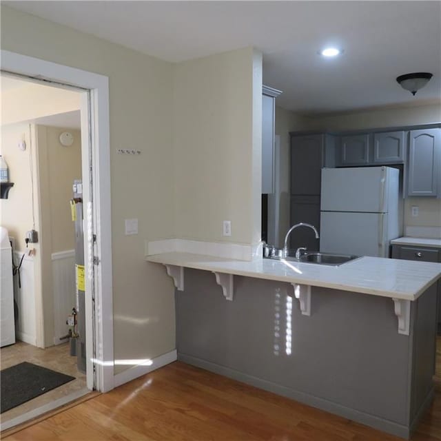 kitchen with sink, light hardwood / wood-style flooring, white refrigerator, kitchen peninsula, and a kitchen bar