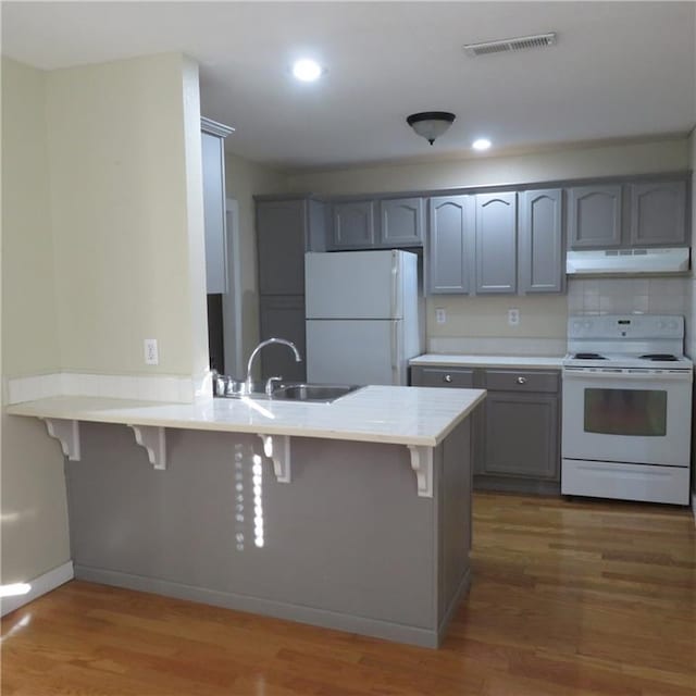 kitchen with a kitchen bar, white appliances, kitchen peninsula, and dark wood-type flooring