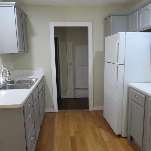 kitchen with gray cabinets, white fridge, light hardwood / wood-style floors, and sink