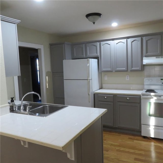 kitchen with sink, range hood, kitchen peninsula, white appliances, and hardwood / wood-style flooring