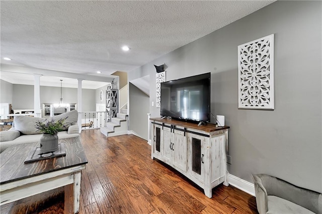 living room featuring lofted ceiling, ornate columns, an inviting chandelier, a textured ceiling, and hardwood / wood-style floors