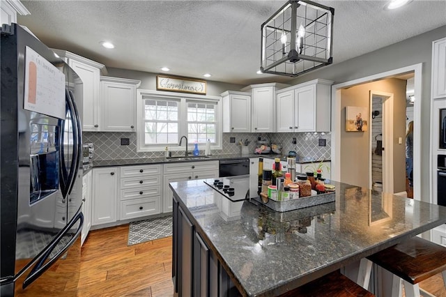 kitchen with pendant lighting, white cabinetry, a kitchen island, and black appliances