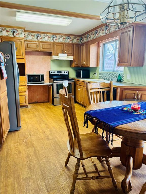 kitchen with pendant lighting, backsplash, light hardwood / wood-style flooring, appliances with stainless steel finishes, and a notable chandelier