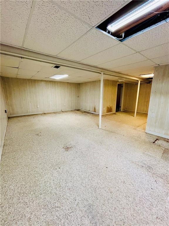 basement with a paneled ceiling, light colored carpet, and wooden walls