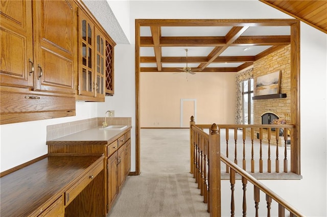 kitchen with sink, beam ceiling, coffered ceiling, light carpet, and a stone fireplace