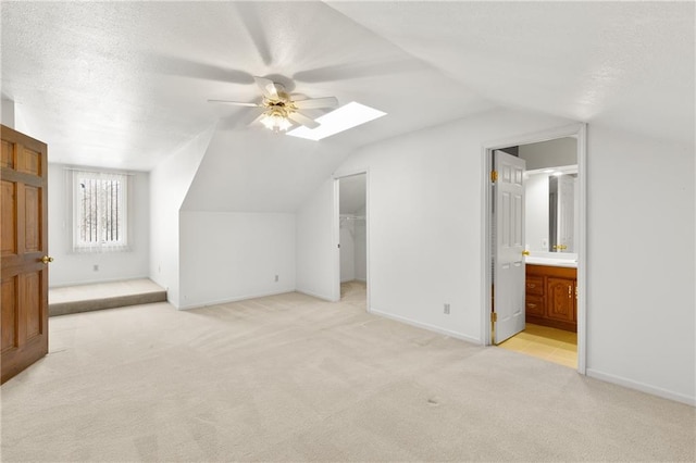 bonus room featuring ceiling fan, lofted ceiling with skylight, and light carpet