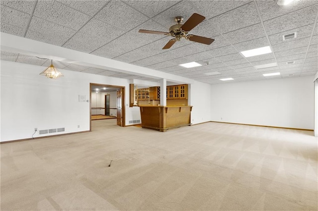 unfurnished living room featuring carpet flooring, a drop ceiling, bar area, and ceiling fan