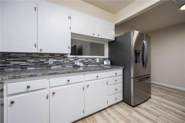 kitchen featuring stainless steel fridge, backsplash, white cabinetry, and dark stone counters