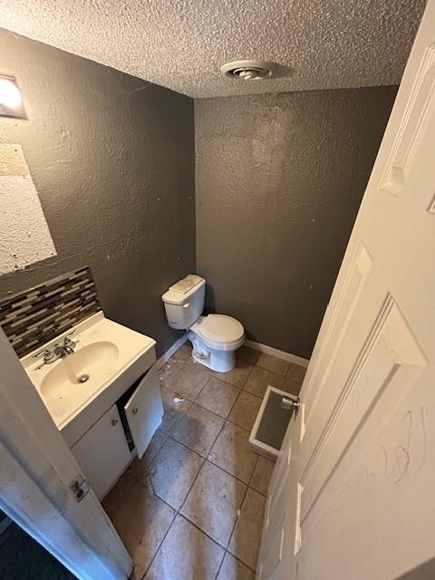 bathroom featuring tile patterned flooring, a textured ceiling, vanity, and toilet