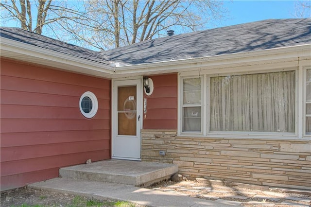 doorway to property with stone siding and roof with shingles