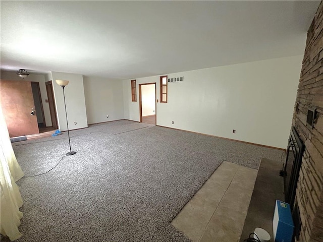 unfurnished living room with carpet floors, baseboards, a stone fireplace, and visible vents