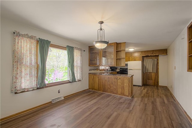 kitchen featuring brown cabinetry, visible vents, open shelves, freestanding refrigerator, and a peninsula