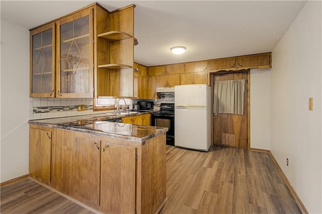 kitchen with a sink, light wood-style floors, a peninsula, backsplash, and black appliances