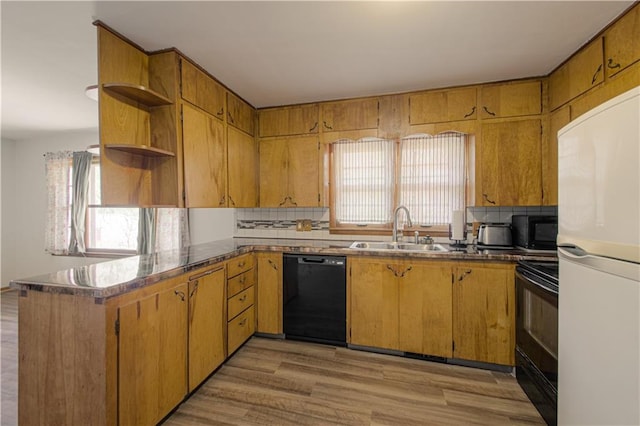 kitchen featuring open shelves, a sink, light wood-style flooring, a peninsula, and black appliances