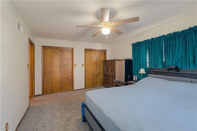 carpeted bedroom with multiple closets, visible vents, and ceiling fan