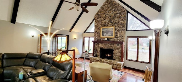 living room featuring hardwood / wood-style floors, plenty of natural light, a stone fireplace, and beam ceiling