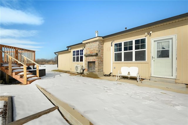 snow covered rear of property with ac unit, a patio, and an outdoor stone fireplace