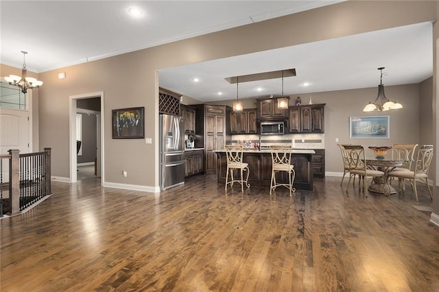 kitchen with stainless steel appliances, dark wood-type flooring, a kitchen island with sink, a breakfast bar, and dark brown cabinets