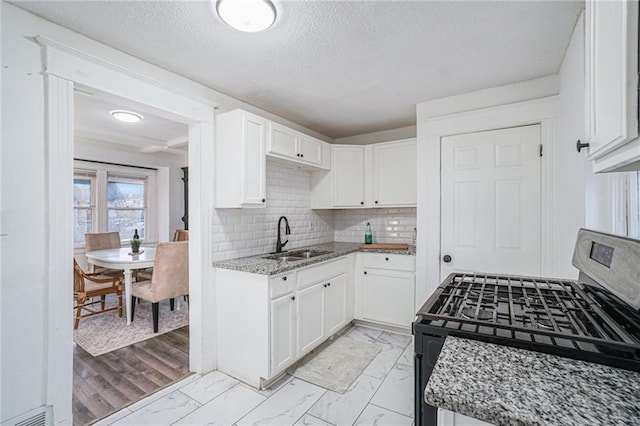 kitchen featuring sink, light stone counters, black gas stove, decorative backsplash, and white cabinets