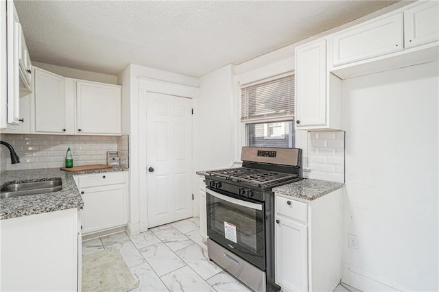 kitchen featuring sink, stainless steel gas stove, tasteful backsplash, light stone counters, and white cabinetry