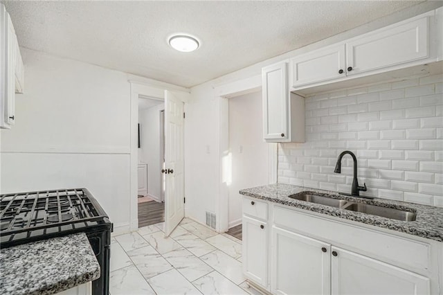 kitchen featuring white cabinets, sink, light stone countertops, and backsplash