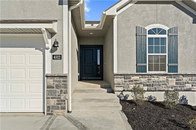 entrance to property with a garage, stone siding, and stucco siding