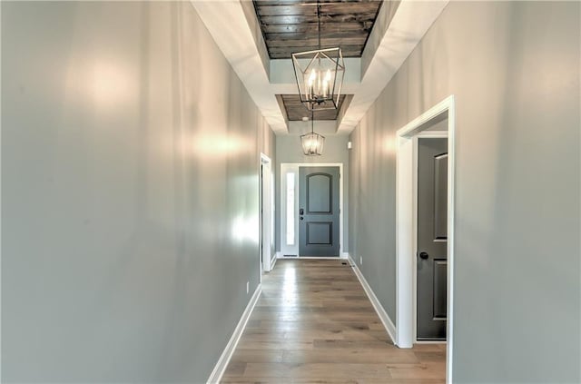 hall featuring a notable chandelier, baseboards, and wood finished floors