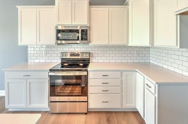 kitchen with stainless steel appliances, light countertops, light wood-style floors, white cabinetry, and tasteful backsplash