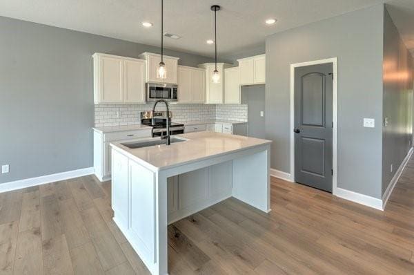 kitchen with decorative backsplash, stainless steel microwave, white cabinets, and a center island with sink