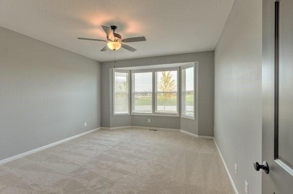 unfurnished room with a ceiling fan, baseboards, and light carpet