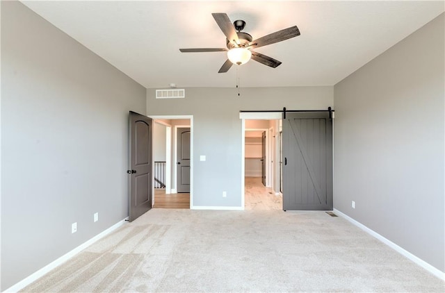 unfurnished bedroom featuring light carpet, visible vents, baseboards, and a barn door