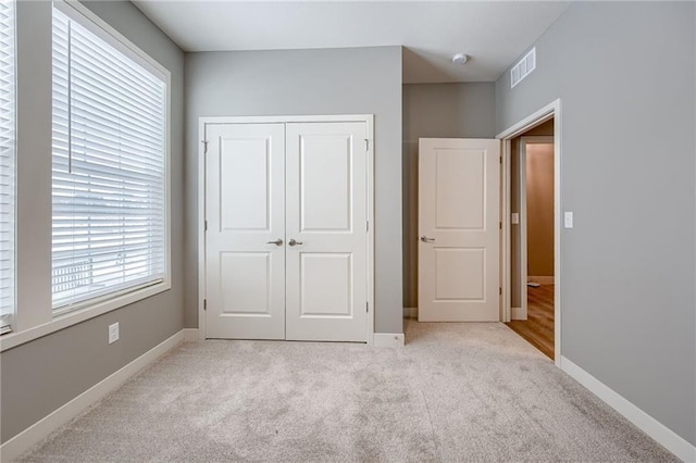 unfurnished bedroom with a closet, visible vents, light colored carpet, and baseboards